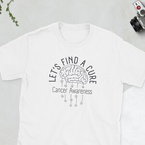 May include: White t-shirt with a black and white graphic design of a brain with the text "Let's Find A Cure" and "Cancer Awareness" below the brain.