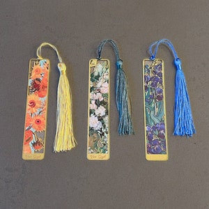 May include: Four gold-colored metal bookmarks with colorful floral designs and tassels. The bookmarks feature artwork by Vincent van Gogh. The tassels are yellow, teal, and blue.