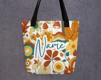 May include: A white tote bag with black handles. The bag features a retro-style design with mushrooms, leaves, flowers, and swirls in shades of orange, yellow, and green. The word "Name" is written in cursive on the bag.
