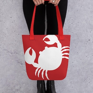 May include: Red tote bag with a white crab silhouette design. The bag has red handles.