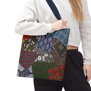 May include: A patchwork tote bag with a variety of patterned fabric squares in shades of red, green, blue, and brown. The bag has a dark blue strap and is held by a person. The bag's design includes floral, geometric, and paisley patterns.
