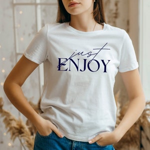 May include: White t-shirt with a navy blue graphic that says "just ENJOY" in a cursive font.
