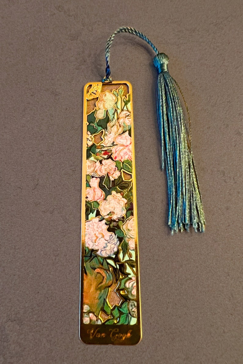 May include: Gold metal bookmark with a floral design featuring pink and white flowers, green leaves, and a gold border. The bookmark has a blue tassel and the text "Van Gogh" at the bottom.