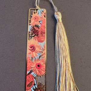 May include: Gold metal bookmark featuring a painting of sunflowers by Vincent van Gogh. The bookmark has a tassel.