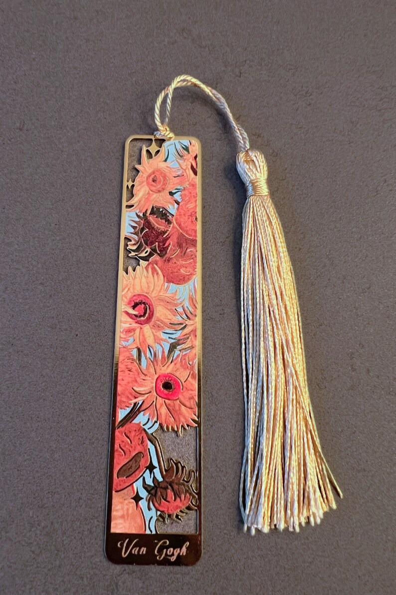 May include: Gold metal bookmark featuring a painting of sunflowers by Vincent van Gogh. The bookmark has a tassel.