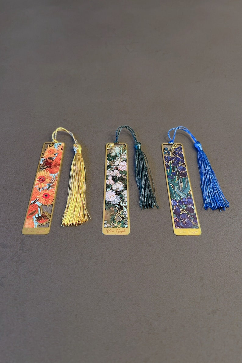 May include: Four gold bookmarks with colorful floral designs and tassels. The bookmarks feature artwork by Van Gogh. The tassels are yellow, green, and blue.