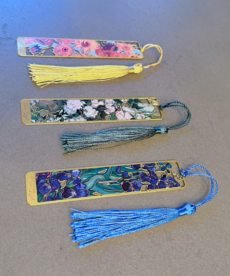 May include: Set of three gold-toned bookmarks with colorful floral designs and tassels. Each bookmark features a different floral painting and the artist's name, "Van Gogh", is printed on the bottom. The tassels are yellow, green, and blue.