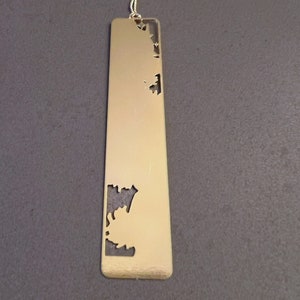 May include: A gold metal bookmark with a decorative cut-out design. The bookmark has a tassel attached to the top.