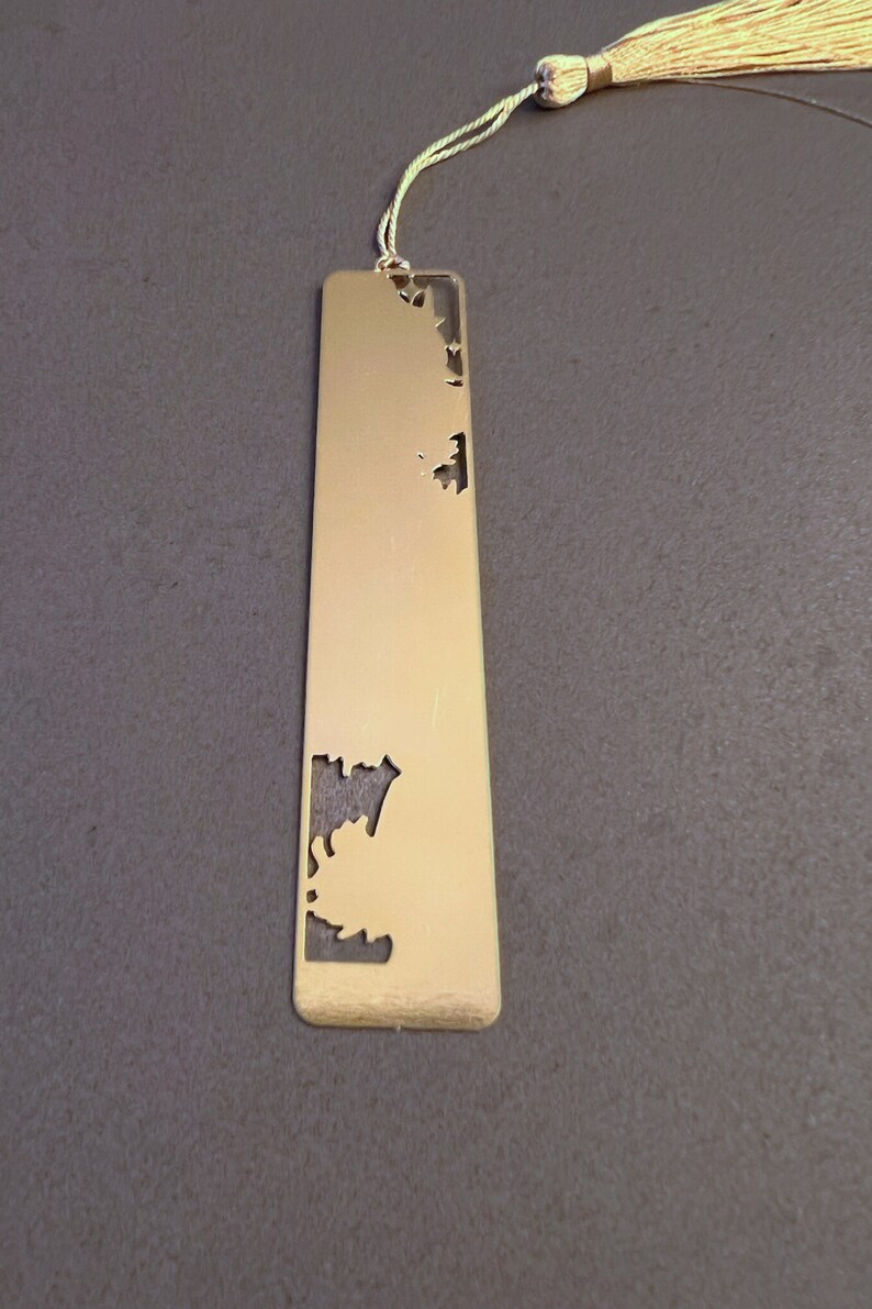 May include: A gold metal bookmark with a decorative cut-out design. The bookmark has a tassel attached to the top.