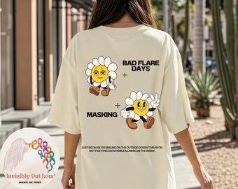 May include: Cream-colored t-shirt featuring daisy cartoon graphics with the phrases "Bad Flare Days" and "Masking." The shirt includes the text: "Just because I'm smiling on the outside doesn't mean I'm not fighting an invisible illness on the inside."