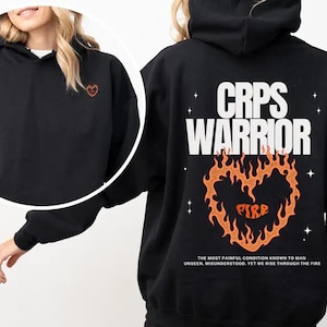 May include: Black hoodie featuring a small embroidered heart on the front and the text "CRPS WARRIOR" on the back. A fiery heart graphic with "FIRE" is below the text. The hoodie also has a quote about rising through the fire.
