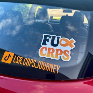 May include: A red car window features two stickers. The top sticker says "FUC CRPS" in white and orange. The bottom sticker, in an orange rectangle, reads "LSR.CRPS.JOURNEY" with a musical note symbol.
