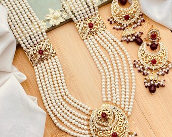 May include: A multi-strand pearl necklace with a large, ornate pendant and matching earrings. The pendant and earrings are gold-toned and feature intricate designs with red and white stones.