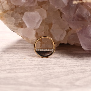 Puede incluir: Anillo de septum de oro con una incrustación de abulón blanco y negro y una fila de piedras de circonita cúbica transparentes.