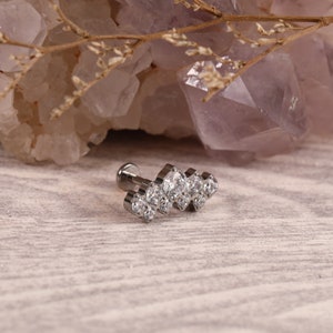 Könnte beinhalten: Ein silbernes Körperschmuckstück mit einer Reihe von klaren Zirkonia-Steinen. Das Stück ist für das Tragen in einem Knorpelpiercing gedacht.