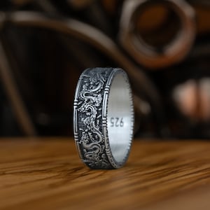 May include: A silver ring with an intricate design of dragons and floral patterns. The ring is engraved with the number "925" on the inside.