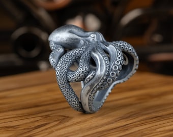 May include: A silver octopus ring with detailed tentacles. The ring is on a wooden surface.