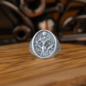 May include: A silver ring with an oval-shaped design featuring a woman standing in a forest with a full moon in the background.