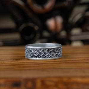 May include: A silver ring with a geometric pattern. The ring is on a wooden surface.