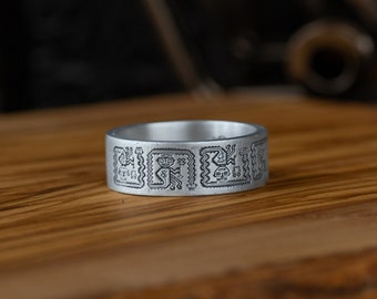 May include: A silver ring with an intricate design engraved on the band. The design features geometric patterns and stylized figures.