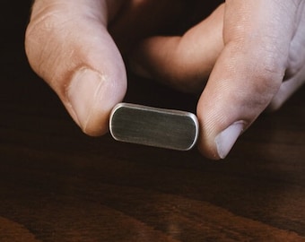 May include: A silver metal bar with rounded edges, held between two fingers.
