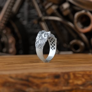 Op de afbeelding: Een zilveren ring met een leeuwenkopontwerp. De ring is gedetailleerd met een getextureerde manen en een geometrisch patroon op de band.