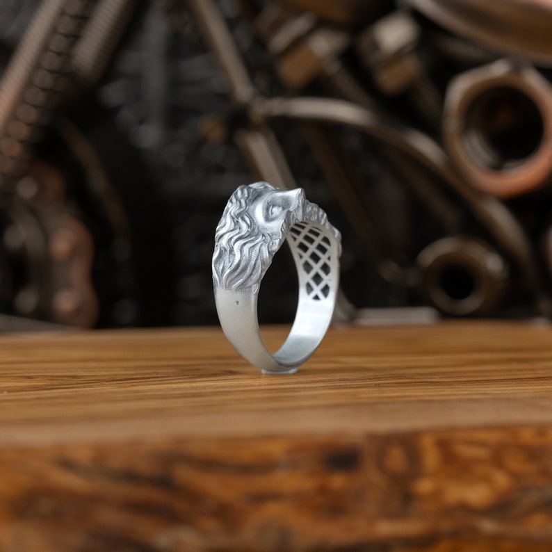 Op de afbeelding: Een zilveren ring met een leeuwenkopontwerp. De ring is gedetailleerd met een getextureerde manen en een geometrisch patroon op de band.