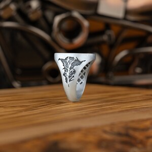 May include: A silver ring with a tree design. The ring is on a wooden surface.