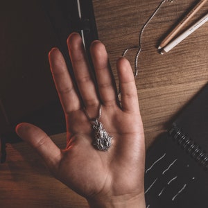 May include: A silver necklace with a pendant featuring a detailed design of a woman's face. The pendant is hanging from a silver chain.