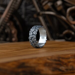 May include: A silver ring with a textured design of swirling clouds. The ring is marked with the number "925" on the inside.