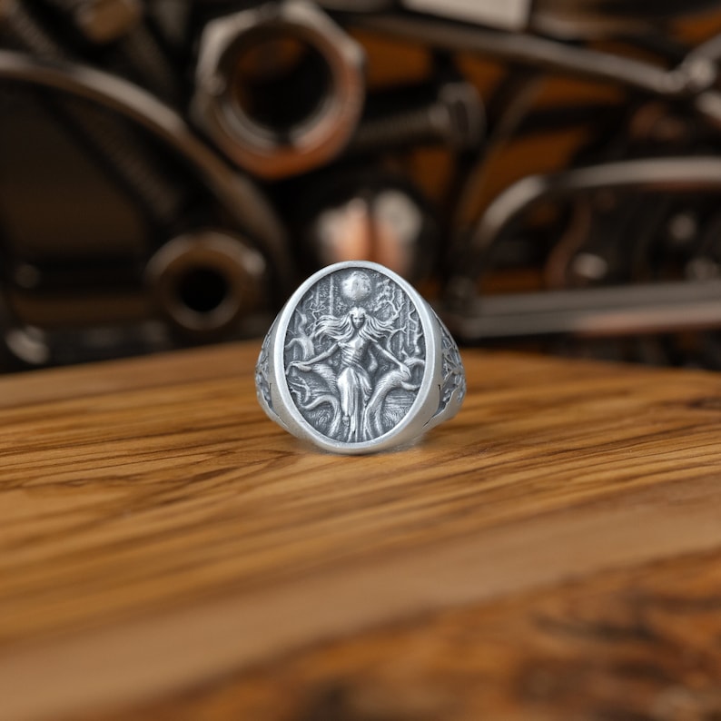 May include: A silver ring with an oval-shaped design featuring a woman standing in a forest with a full moon in the background.