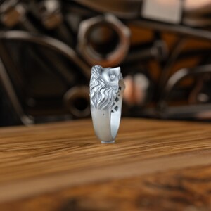 Op de afbeelding: Een zilveren ring met een gedetailleerd ontwerp van een leeuwenkop. De ring wordt van de zijkant getoond, met de leeuwenkop naar de kijker gericht.