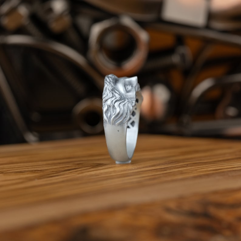 Op de afbeelding: Een zilveren ring met een gedetailleerd ontwerp van een leeuwenkop. De ring wordt van de zijkant getoond, met de leeuwenkop naar de kijker gericht.