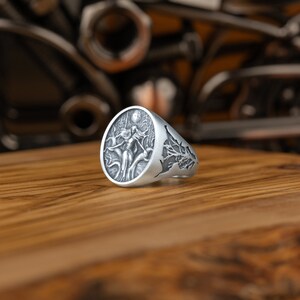 May include: A silver ring with an oval-shaped design featuring a woman standing in a tree with a full moon in the background.