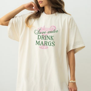 May include: A white oversized t-shirt with a pink margarita glass graphic and the text "Save water drink margs" in green.