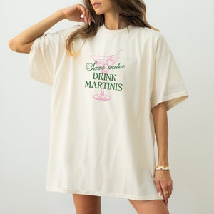 May include: A white oversized t-shirt with a pink martini glass graphic and the text "Save water drink martinis" in green.