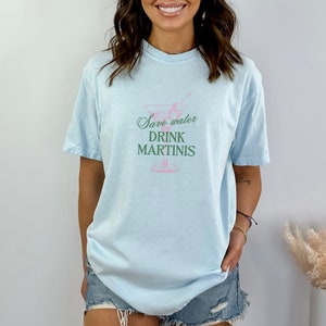 May include: A light blue t-shirt with a martini glass graphic and the text "Save water drink martinis" in pink and green.
