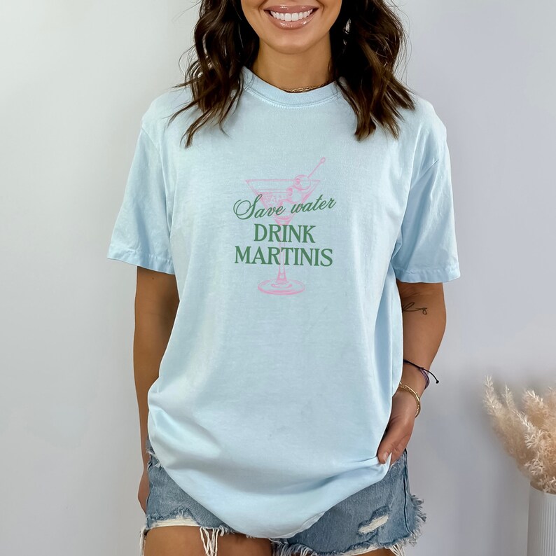 May include: A light blue t-shirt with a martini glass graphic and the text "Save water drink martinis" in pink and green.