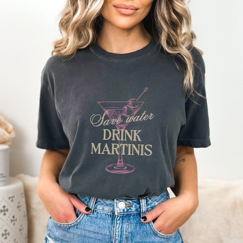 May include: A dark gray t-shirt with a pink martini glass graphic and the text "Save water drink martinis" in a beige font.