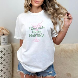 May include: White t-shirt with a pink martini glass graphic and the text "Save water drink martinis" in green.