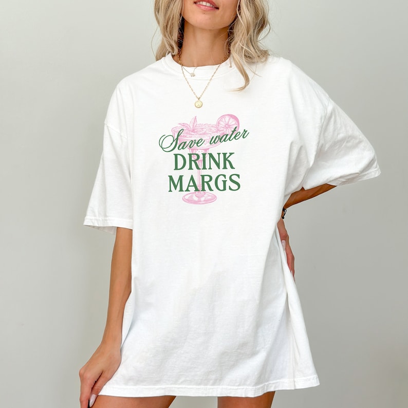 May include: White oversized t-shirt with a green and pink graphic of a margarita glass and the text "Save water drink margs."