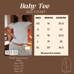 May include: Size chart for a white baby tee with a model wearing the tee in size XS. The chart shows measurements in inches for sizes XS, S, M, L, and XL. The model is 120 lbs, with a 34A bust, 33 inch chest, 27 inch waist, and 32 inch hips.