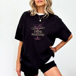 May include: Black oversized t-shirt with a pink martini glass graphic and the text "Save water drink martinis".