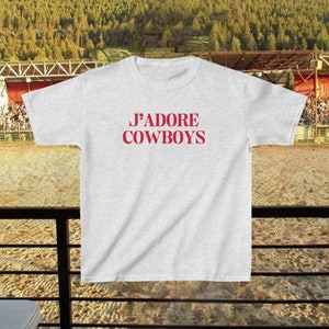 May include: A gray t-shirt with the text "J'ADORE COWBOYS" printed in red.