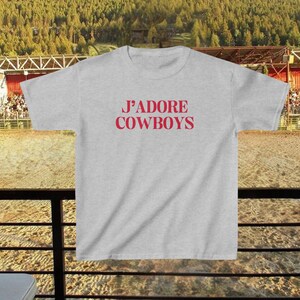 May include: A gray t-shirt with the text "J'ADORE COWBOYS" printed in red on the front.