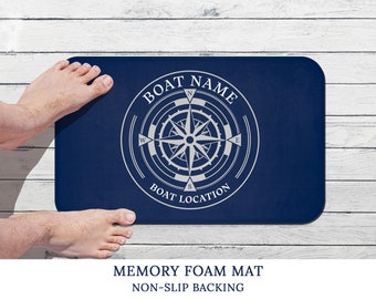May include: A navy blue bath mat with a white compass design and the text "BOAT NAME" and "BOAT LOCATION". The mat is made of memory foam and has a non-slip backing.