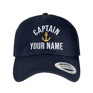 May include: A navy blue baseball cap with white embroidery that reads "Captain" with a yellow anchor and "Your Name".