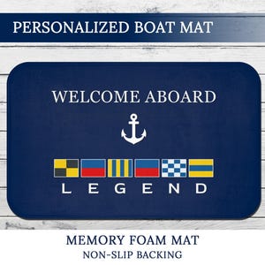 Pode incluir: Tapete de barco azul marinho com as palavras "WELCOME ABOARD" e um gráfico de âncora. A palavra "LEGEND" está abaixo das bandeiras de sinalização. O tapete também tem as palavras "PERSONALIZED BOAT MAT", "MEMORY FOAM MAT" e "NON-SLIP BACKING".