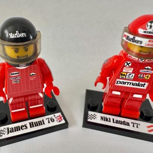 Peut inclure: Deux figurines Lego de pilotes de Formule 1, James Hunt et Niki Lauda, en combinaisons et casques de course rouges. La figurine de James Hunt a un casque noir avec "Marlboro" imprimé dessus. La figurine de Niki Lauda a un casque rouge avec "Marlboro" imprimé dessus. Les deux figurines sont sur des socles noirs.
