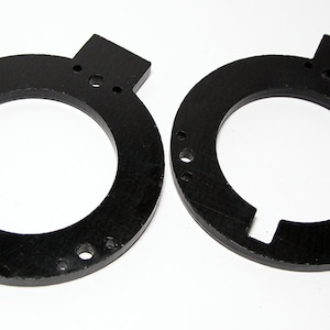 Op de afbeelding: Twee zwarte metalen ringen met een uitsparing aan de zijkant. Elke ring heeft een reeks kleine gaten rond de buitenrand.